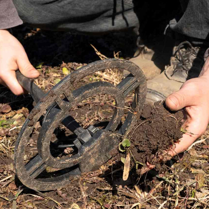 person holding a lump of soil and a metal detector