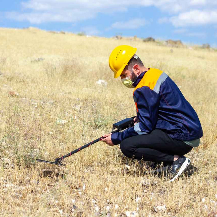 man squatting down holding a metal detector